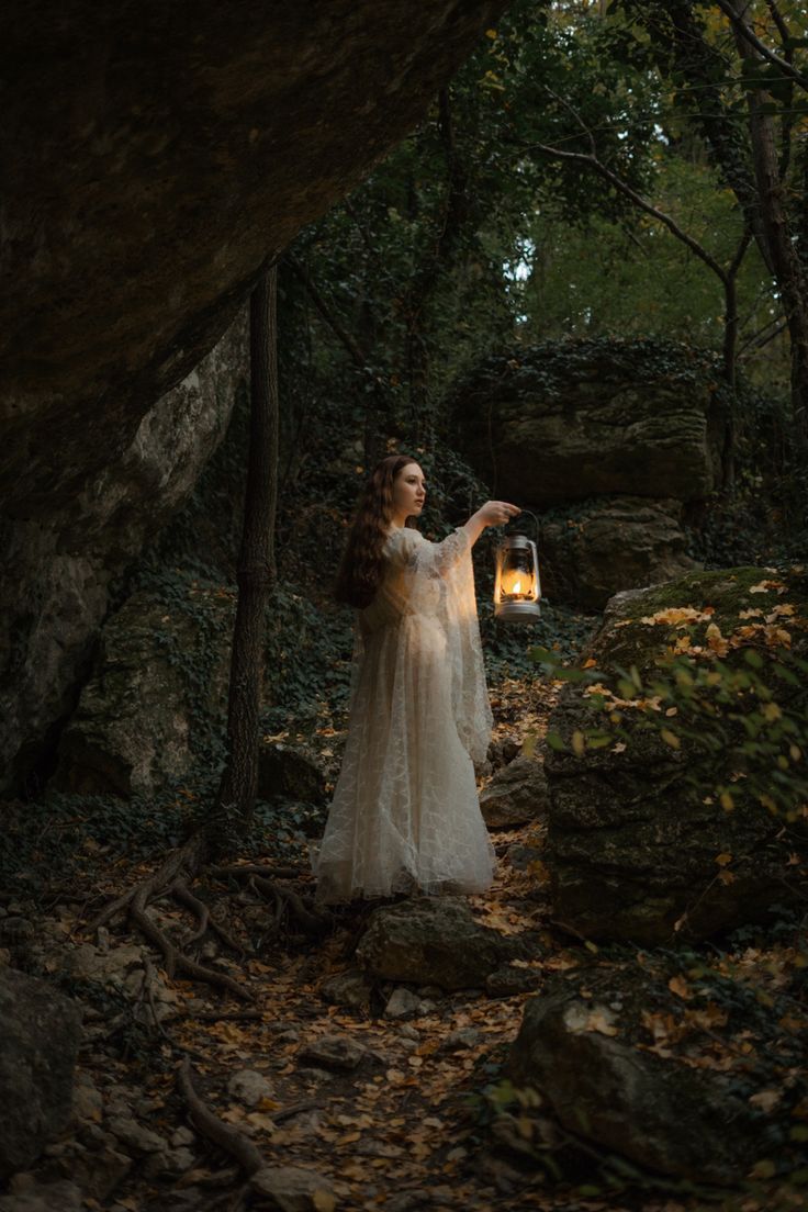 a woman in a white dress is holding a lantern while standing on some rocks and trees