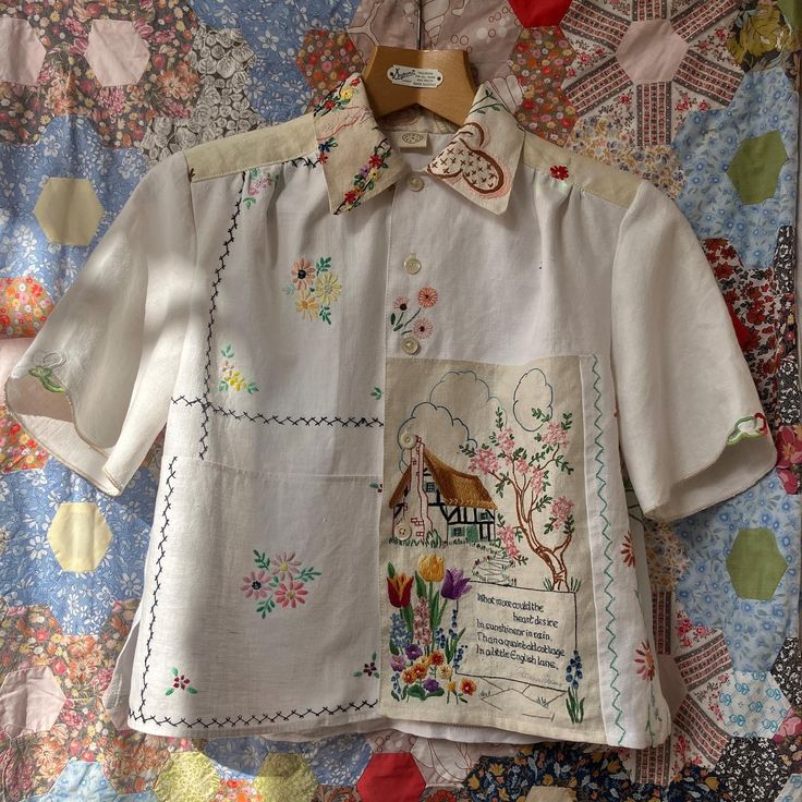 a white shirt with an embroidered design on it and a wooden hanger hanging from the front