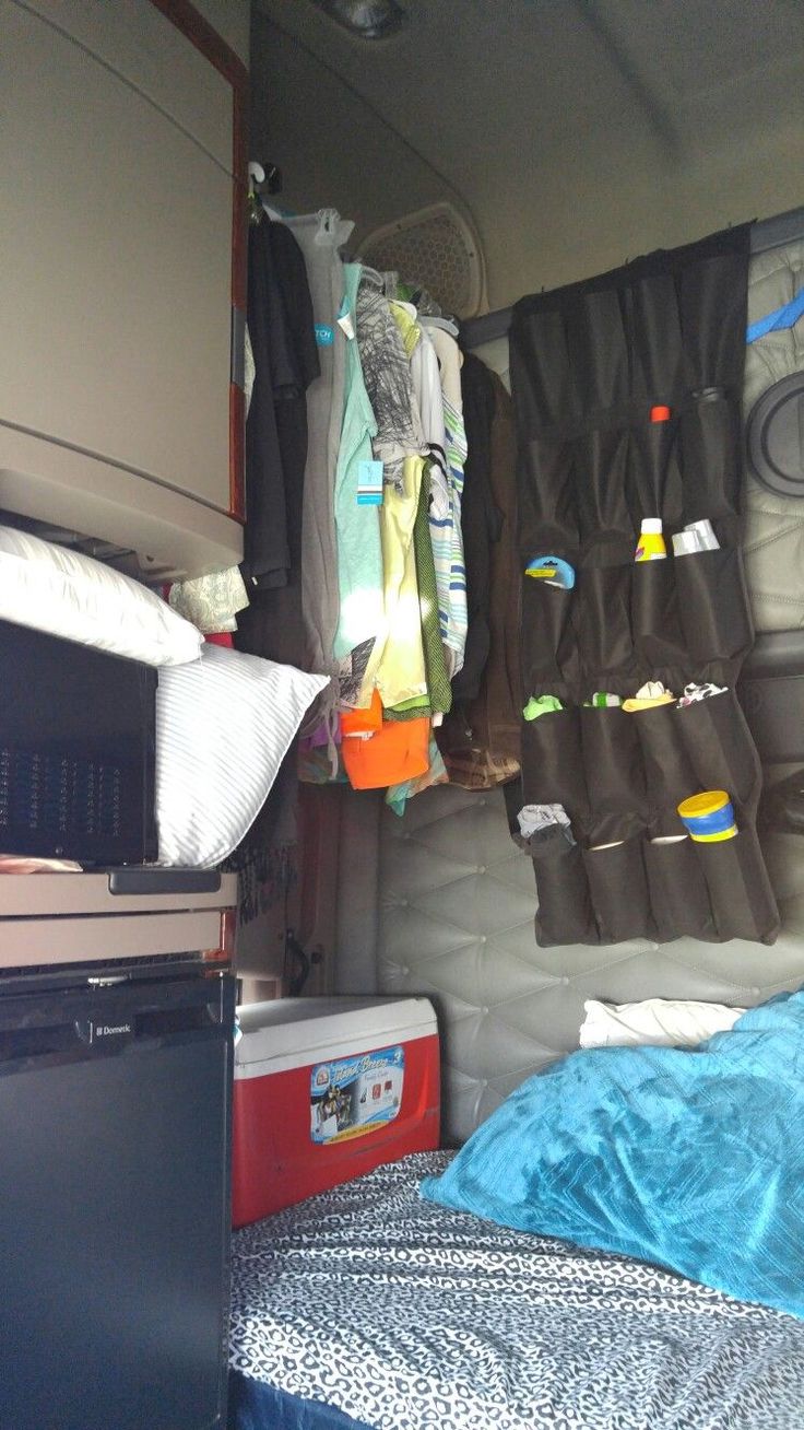 the inside of a camper with clothes hanging from hooks on the wall and a bed in the foreground