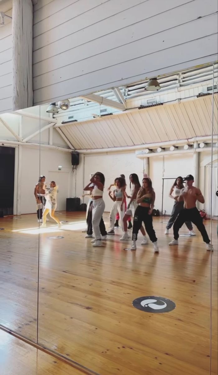 a group of people are dancing on a wooden floor in an indoor dance studio with mirrors