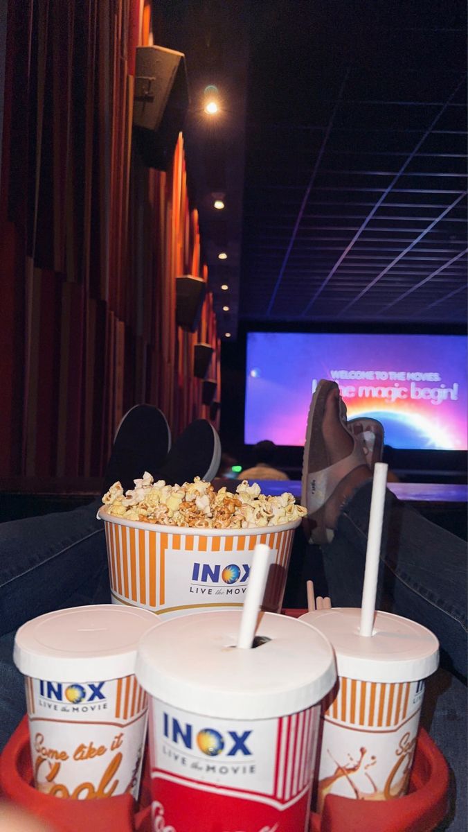 three buckets filled with popcorn sitting on top of a red tray in front of a movie screen