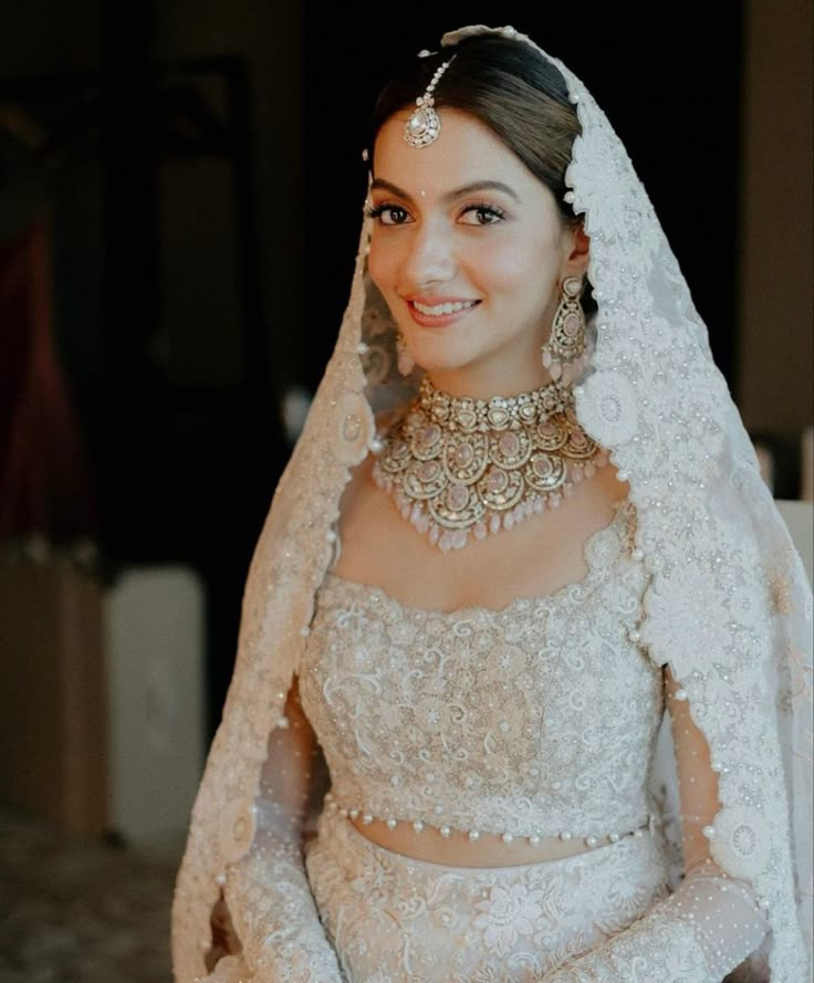 a woman in a white wedding dress and veil with jewels on her head is smiling at the camera