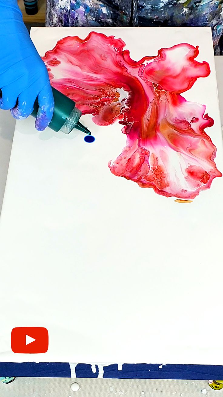 someone in blue gloves is painting a flower with red and pink paint on white paper