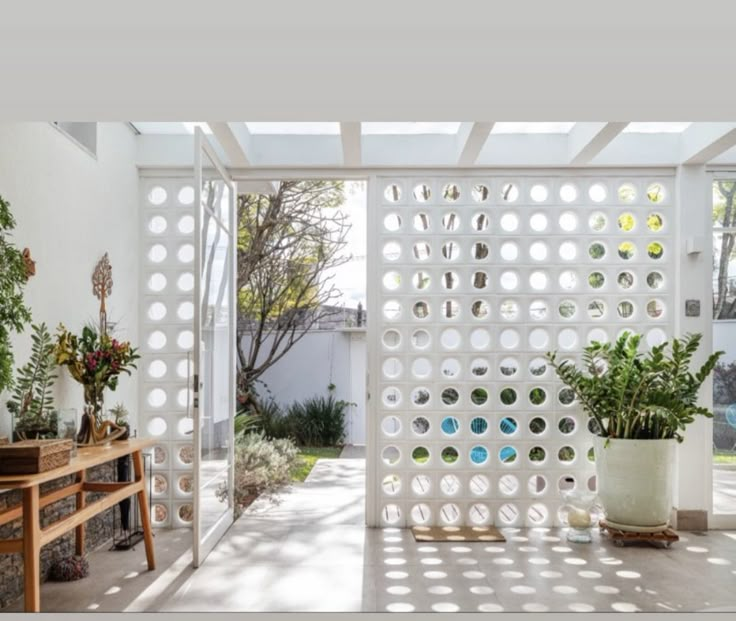 an outdoor room with potted plants and a bench in the foreground is a white pergolated wall