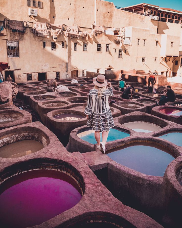 a woman in a hat walking through some water filled barrels with people standing around them