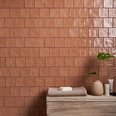 a brown brick wall in a bathroom next to a wooden cabinet with a potted plant on it