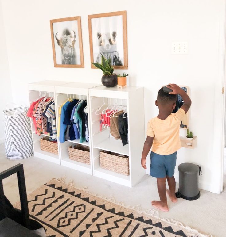 a little boy standing in front of a white shelf