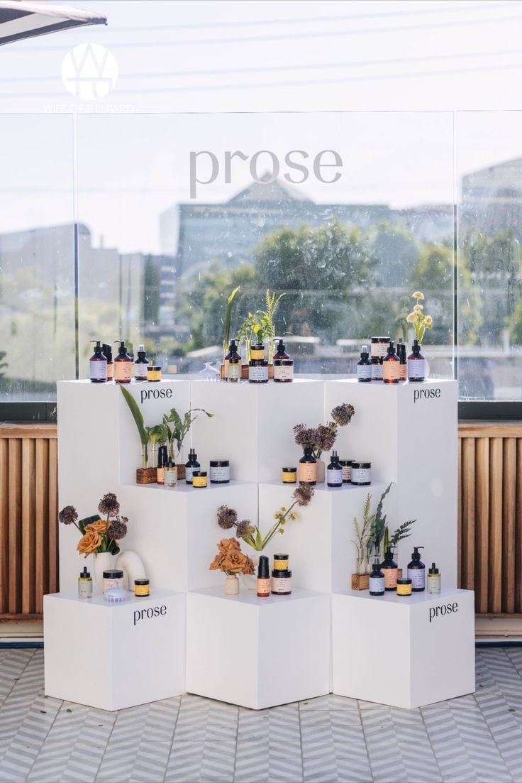 a display case with various bottles and plants on it in front of a window that says prose