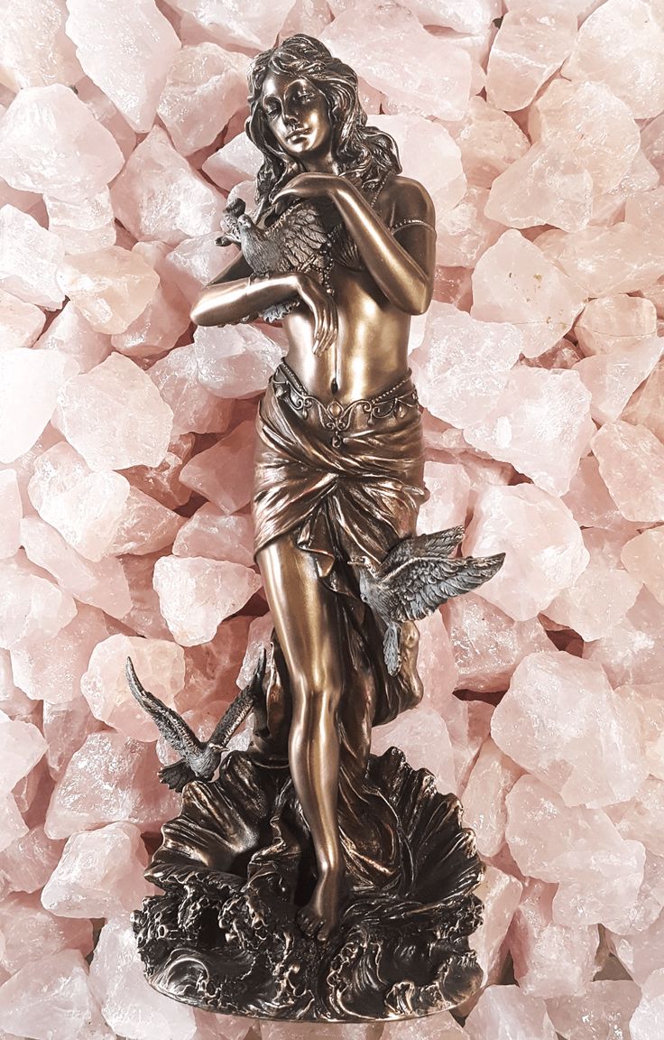 a statue is sitting on some pink crystals in front of a pile of rocks and stones