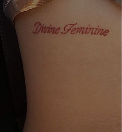 a woman's back with the word divine feminine tattooed on her left side arm