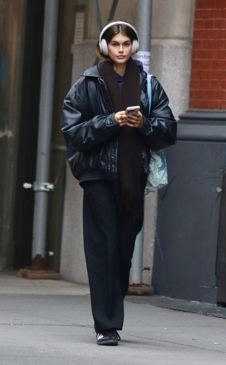 a woman walking down the street while wearing headphones on her head and looking at her cell phone