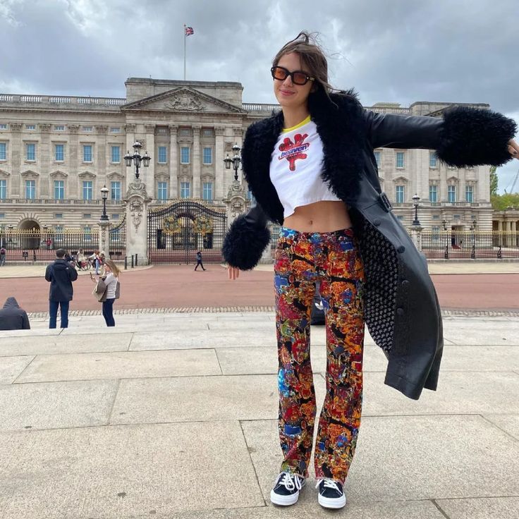 a woman standing in front of a large building wearing colorful pants and a fur coat