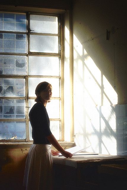 a woman standing in front of a window with sunlight coming through the window panes