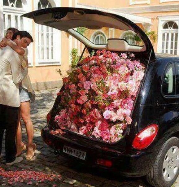 a man and woman standing next to a car with flowers in the trunk