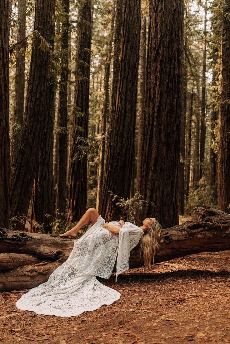 a woman in white dress laying on tree trunk