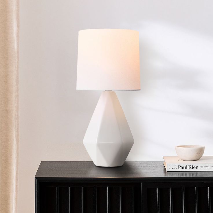 a white lamp sitting on top of a black table next to a book and cup