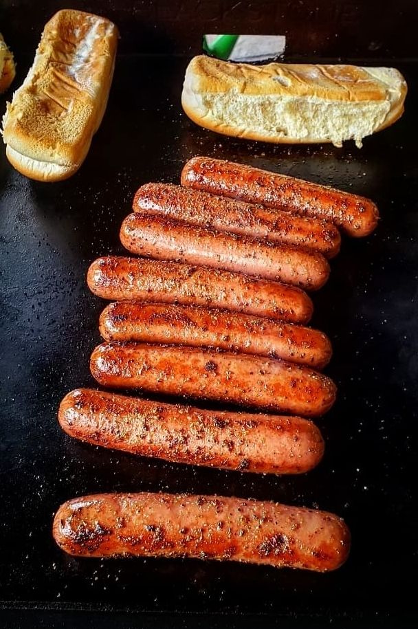 several sausages and bread on a black counter top next to some hotdog buns