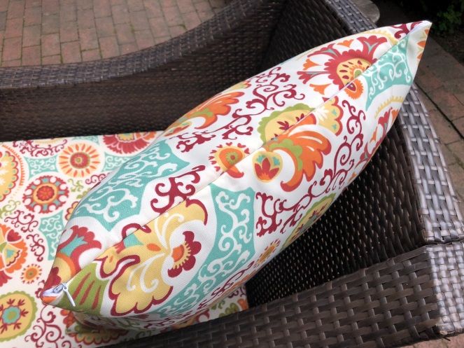 a colorful pillow sitting on top of a chair next to a brick wall and sidewalk