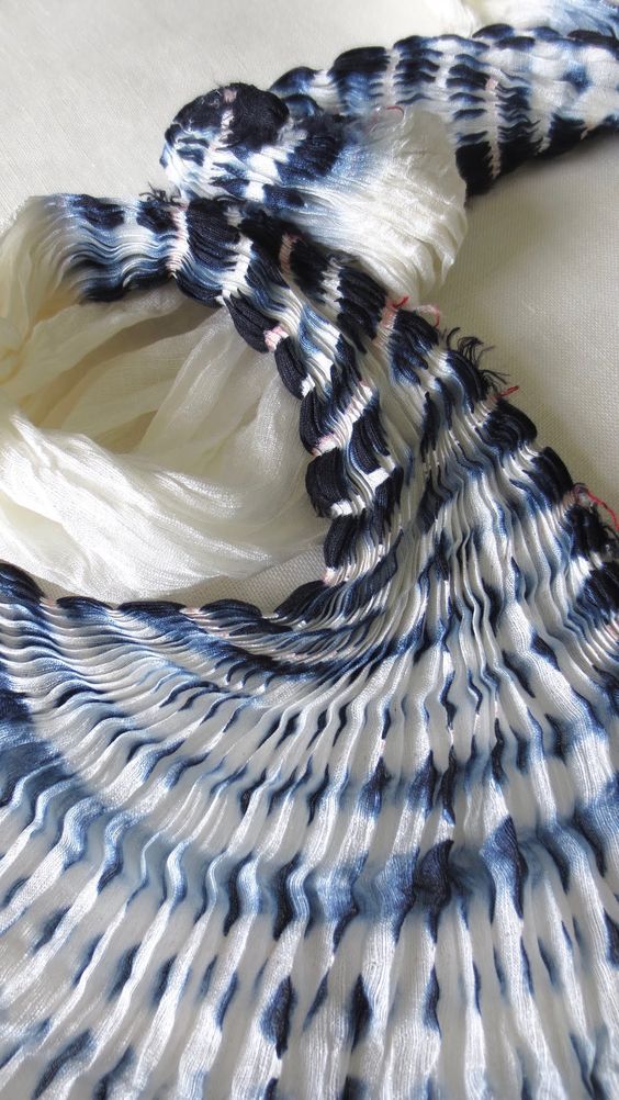 a white and blue tie dyed scarf laying on top of a bed