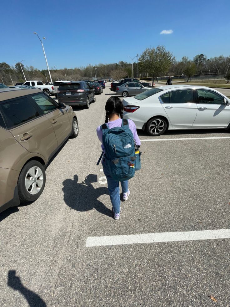 a woman walking across a parking lot next to parked cars