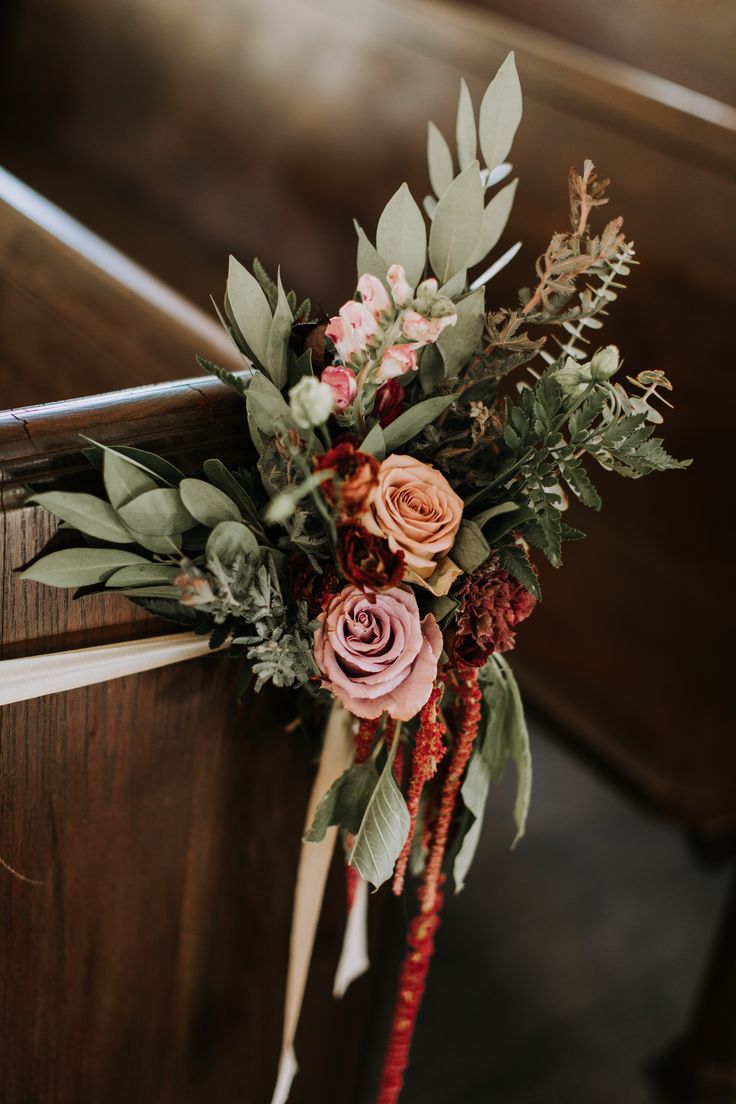 an arrangement of flowers on the back of a wooden church pew with greenery and foliage