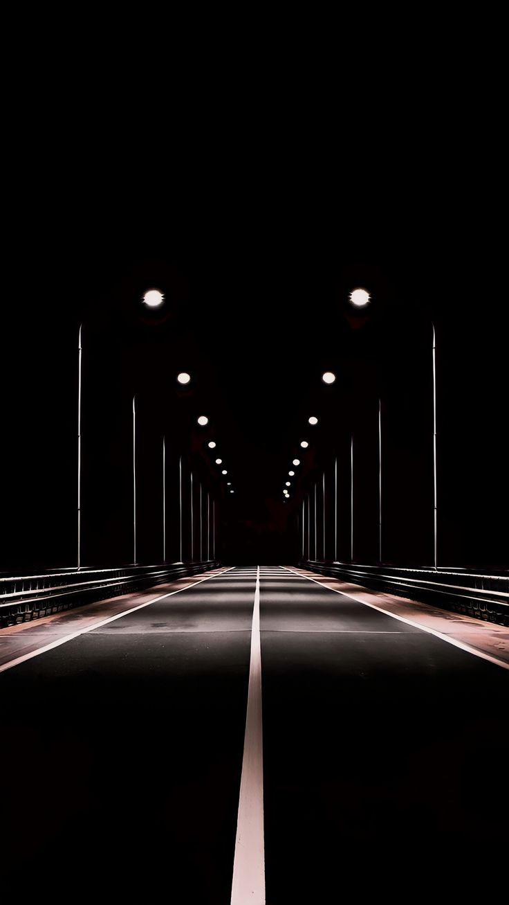 an empty road in the dark with lights on at one end and streetlights above it