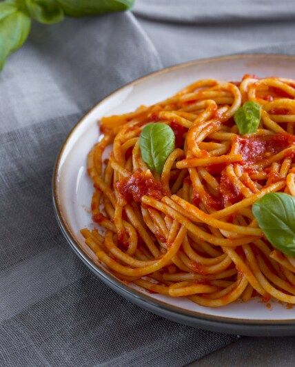 a plate of spaghetti with sauce and basil leaves on the side, ready to be eaten