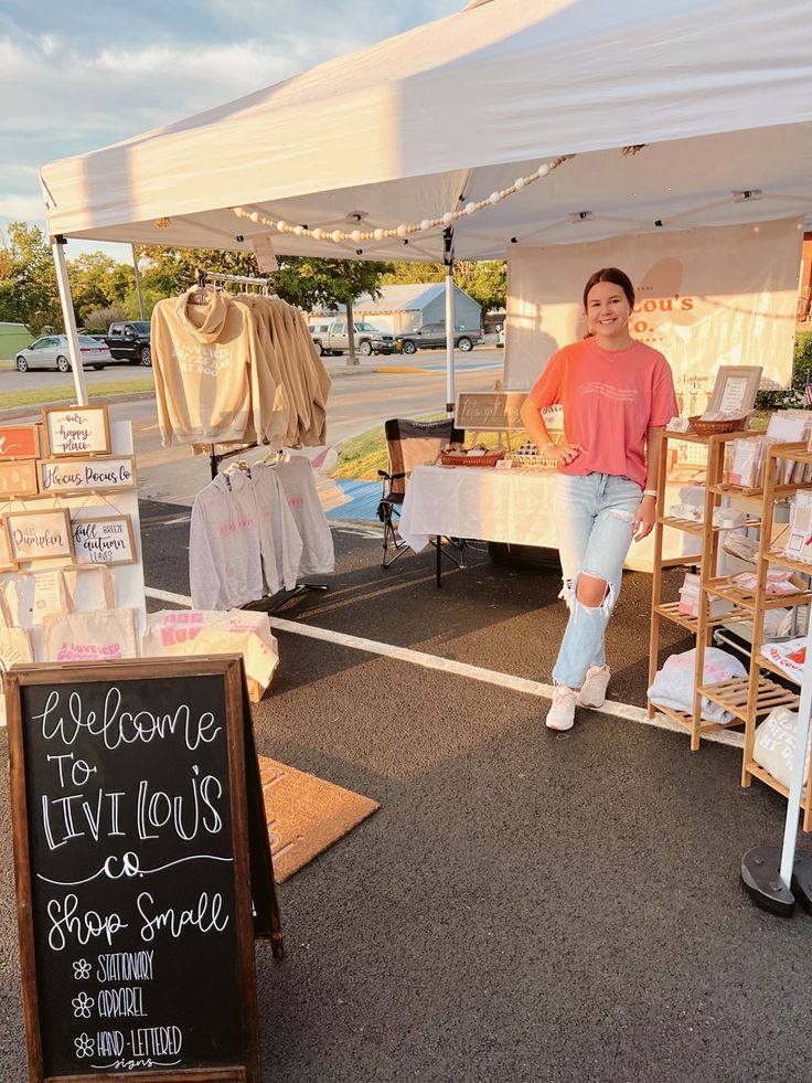 a woman standing in front of a tent selling items