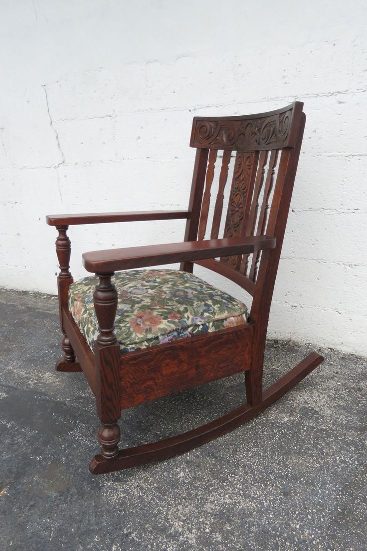 a wooden rocking chair with a floral seat pad on the floor next to a white brick wall