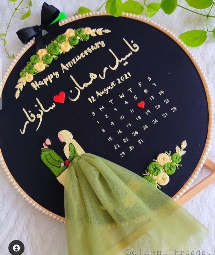 an embroidered wall hanging with a green dress on it's side next to a white table cloth