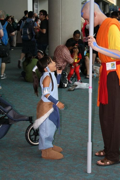 a man in an orange and blue costume standing next to a pole with a small child on it