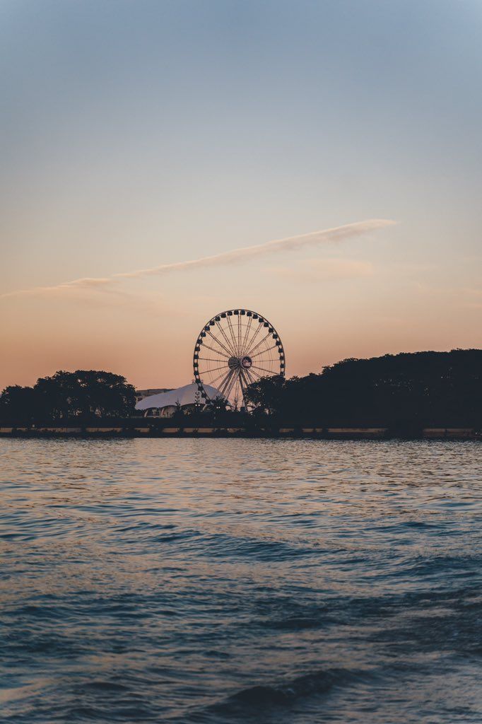 a ferris wheel sitting on top of a large body of water near the ocean at sunset