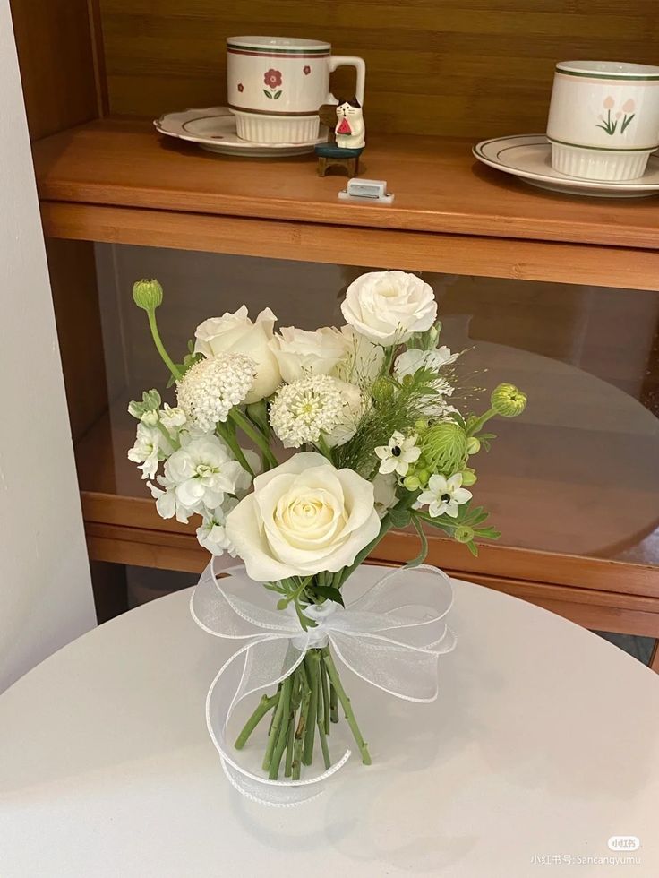 a vase filled with white flowers sitting on top of a table next to cups and saucers