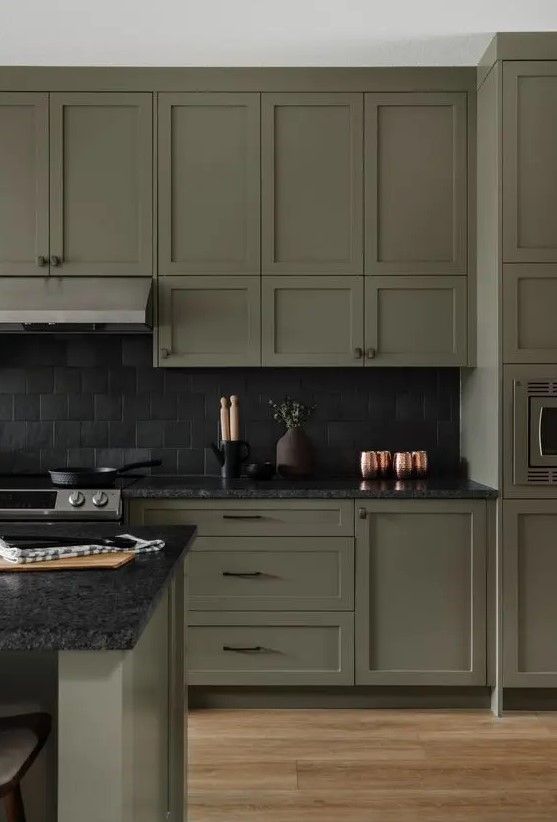 an image of a kitchen setting with green cabinets and black counter tops on the island