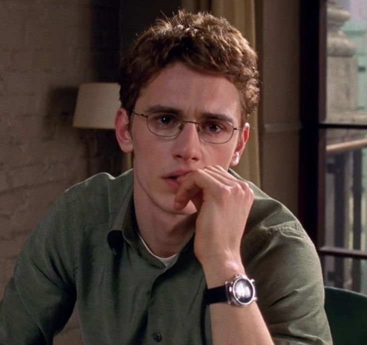 a young man wearing glasses sitting at a table with his hand on his chin and looking off to the side