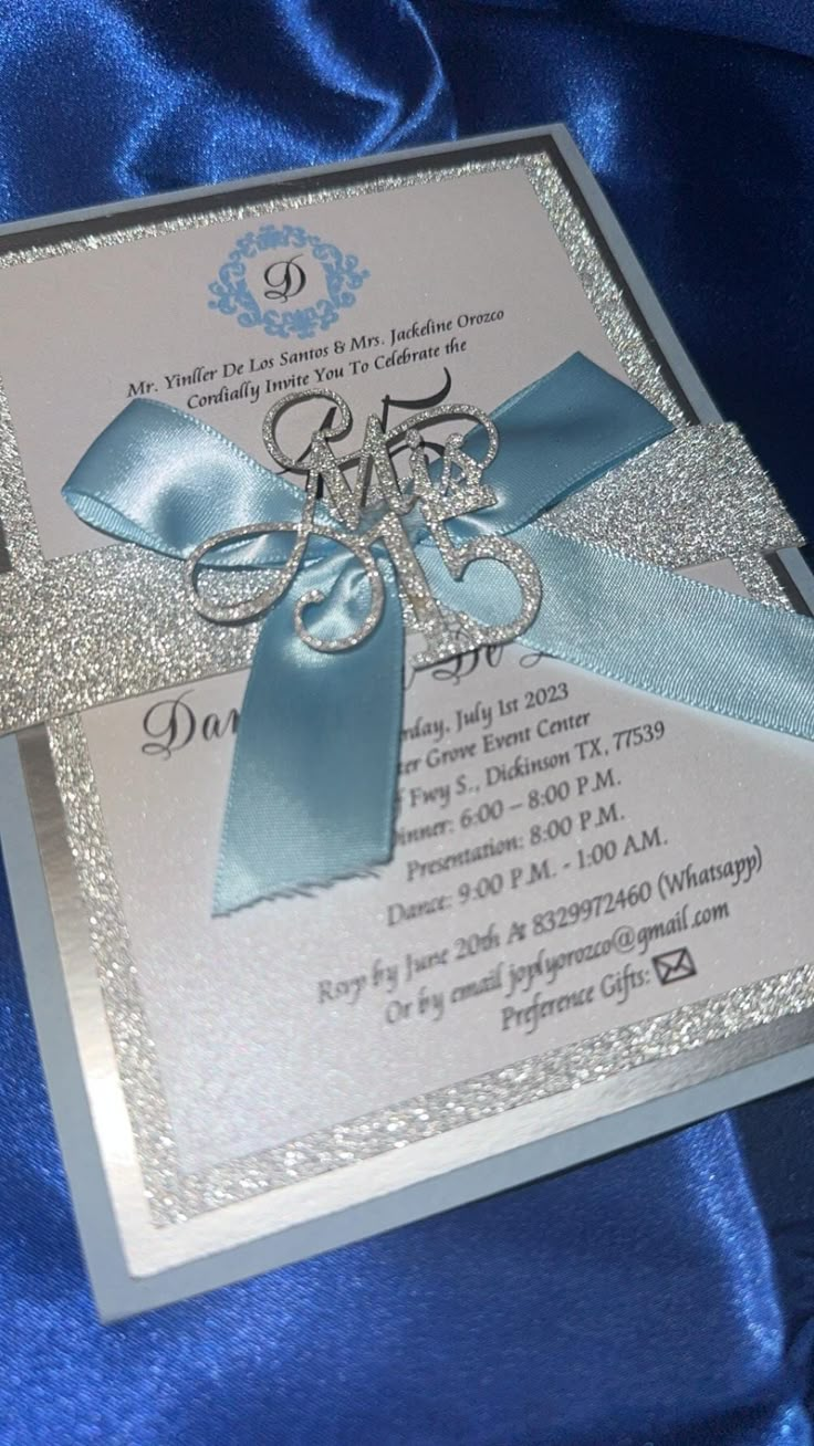 a blue and silver wedding card on a blue satin background with ribbon, scissors and bow