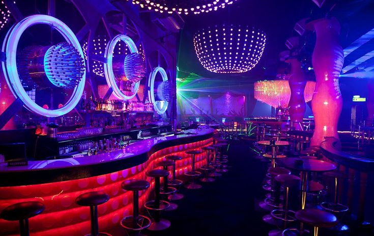 a dimly lit bar with neon lights and circular mirrors on the wall above it, along with stools