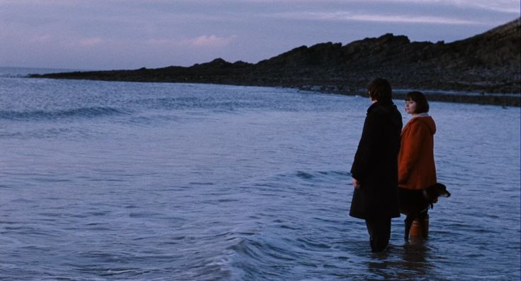 two people standing in the water looking out to sea