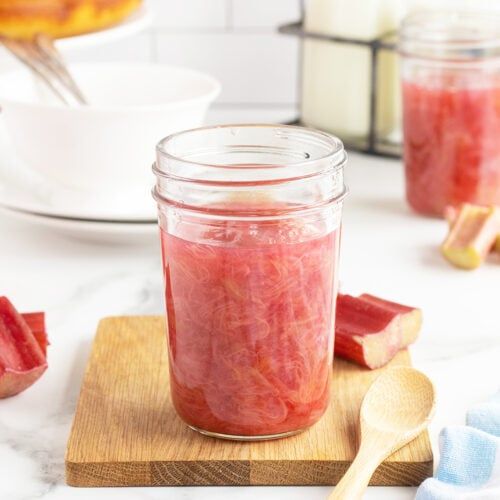 a jar filled with watermelon jam sitting on top of a wooden cutting board