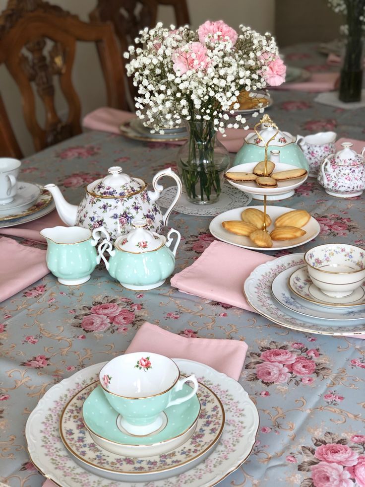 the table is set with tea cups, plates and flowers in vases on it