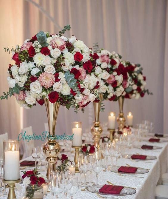 the table is set with white and red flowers in vases, candles, and wine glasses