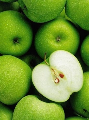 green apples are piled up with one apple sliced in half and the other whole on top