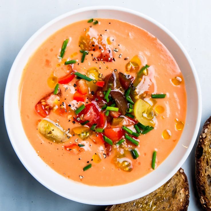 a white bowl filled with soup next to two pieces of bread