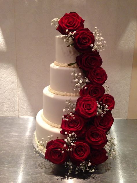 a three tiered wedding cake with red roses on the top and white flowers on the bottom