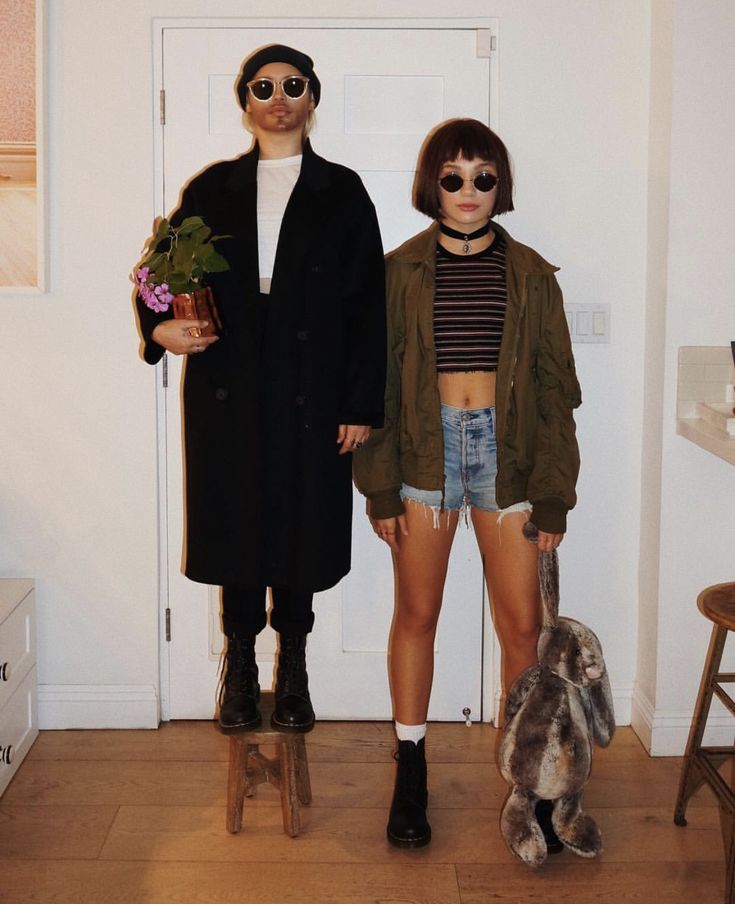 two people standing next to each other in front of a white door and one person holding a potted plant