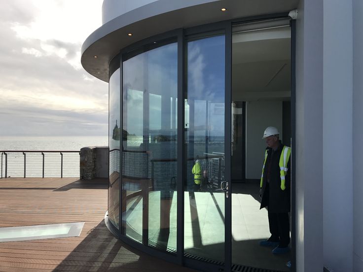 a man standing in front of a glass door on top of a building next to the ocean