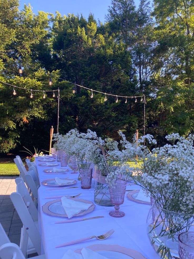 a long table set with white flowers and place settings for an outdoor dinner party in the sun