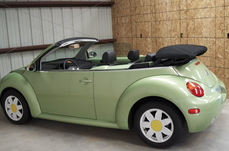 a small green car parked in a garage next to a wooden wall and some windows