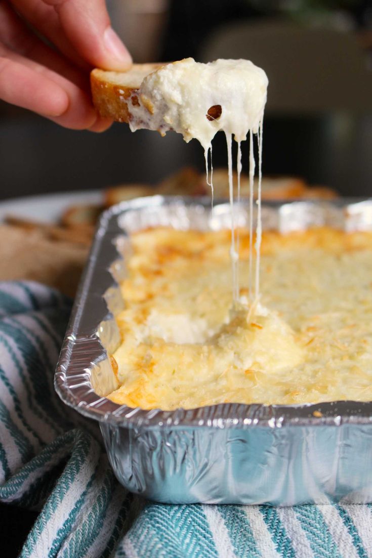 a person dipping cheese on top of a lasagna casserole in a pan