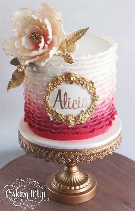 a white and red cake with gold trimmings on a wooden table next to a flower